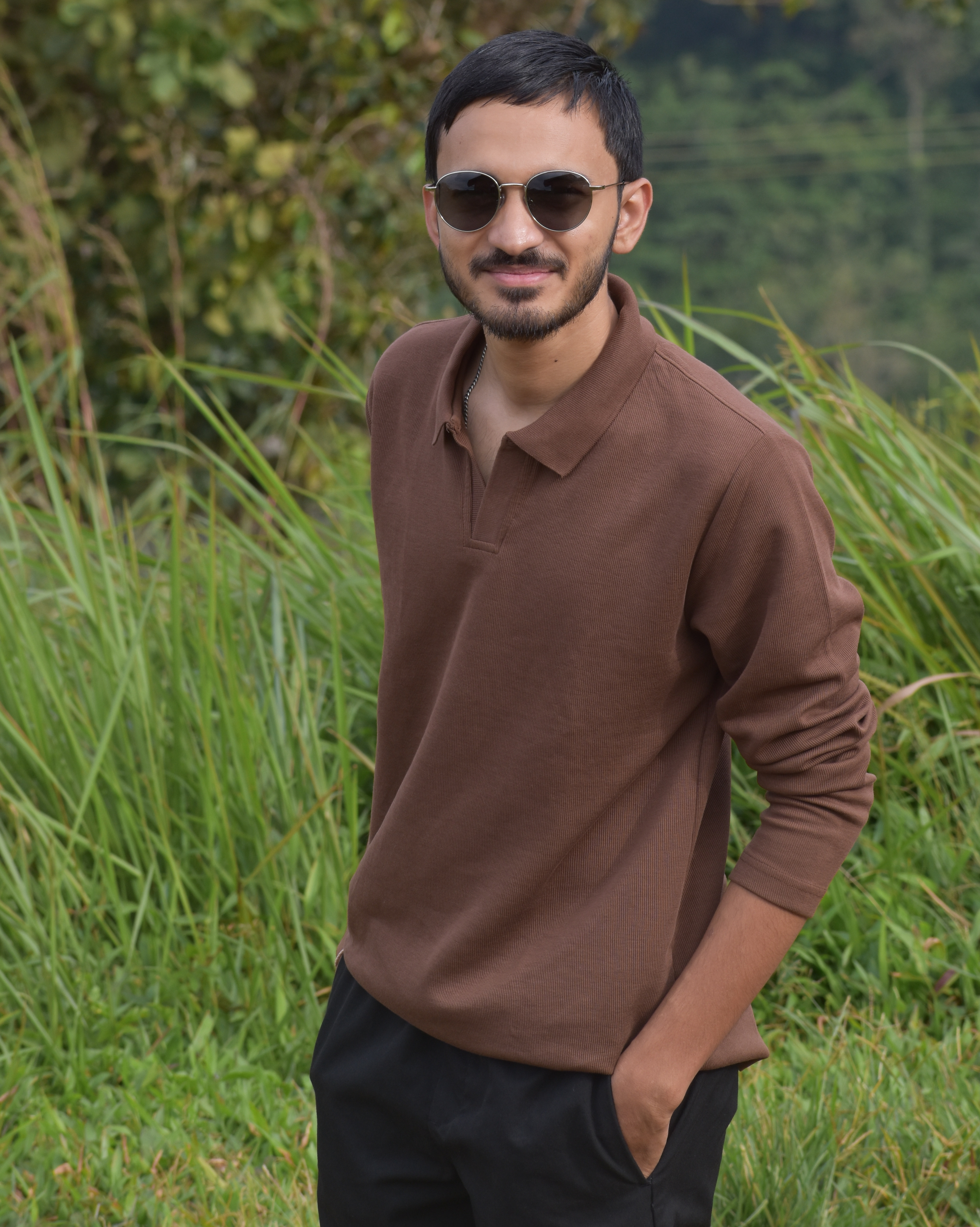 Kartheek standing outdoors in a brown polo and sunglasses.